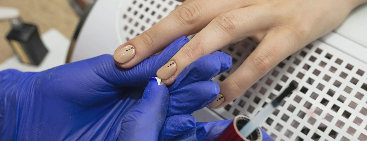 Wykonywanie manicure z&nbsp;użyciem lakieru hybrydowego przez osobę w&nbsp;rękawiczkach ochronnych